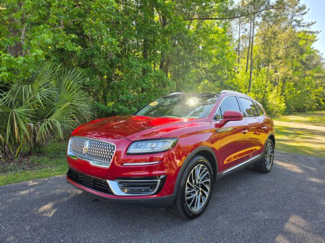 2020 Lincoln Nautilus Reserve Stock #39211 - Car City Services Red Lincoln SUV parked on a sunlit driveway with green trees in the background, front angled toward the camera