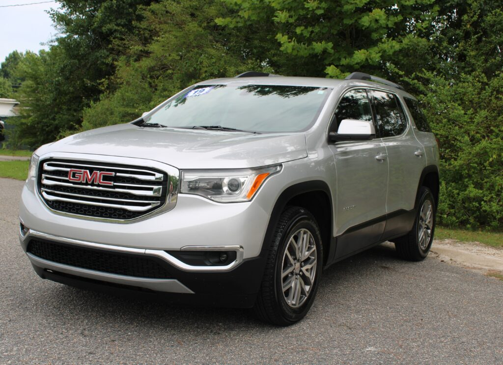 Silver GMC SUV parked on a driveway with lush green trees in the background, front three-quarter view.