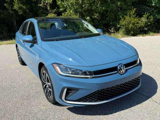 Light blue Volkswagen sedan, front three-quarter view parked on pavement with trees in background
