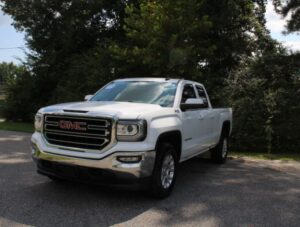 Front three-quarter view of a white GMC pickup truck parked on a paved lot with trees in the background.