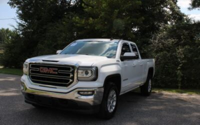 Front three-quarter view of a white GMC pickup truck parked on a paved lot with trees in the background.
