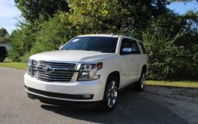 Front, three-quarter view of a white Chevrolet SUV parked on a paved road with trees in the background, sunny day.