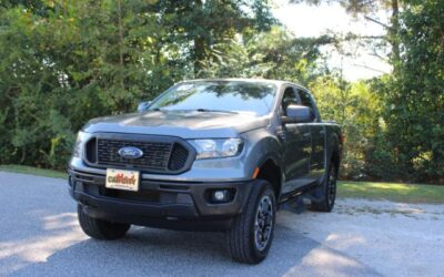 Gray Ford pickup truck parked on a gravel driveway with trees in the background, front-left view.