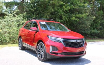 Red Chevrolet SUV parked on a sunny lot with green trees in the background, front three-quarter view.