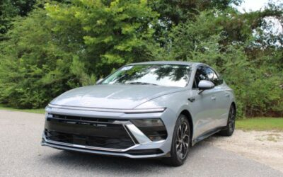 Silver midsize sedan parked on a paved road with green trees in the background.