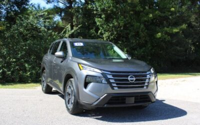 Gray Nissan SUV parked on a paved lot with green trees in the background on a sunny day.