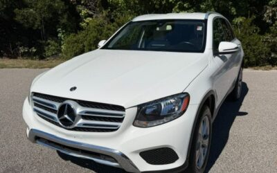 White Mercedes-Benz SUV photographed from a front three-quarter view parked on a paved road with trees in the background,
